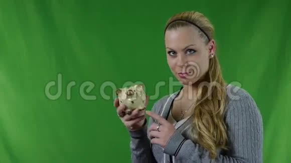 幸福的年轻女人把硬币放在猪的银行与绿色的屏幕视频的预览图