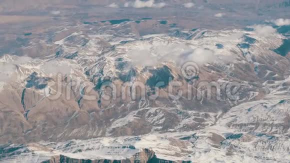 令人惊叹的山脉美景微微覆盖着雪从云中掠过从飞机窗口眺望视频的预览图