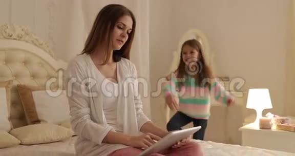 母亲与女儿同床共枕用平板电脑快乐微笑年轻家庭视频的预览图