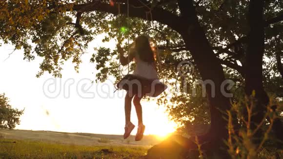 孩子们骑着绳子在森林里的橡树树枝上摇摆女孩笑高兴年轻女孩在树下荡秋千视频的预览图