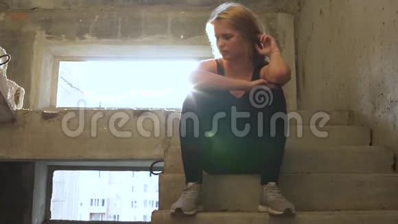 年轻不幸的女孩正坐在一栋废弃的大楼里的楼梯上视频的预览图
