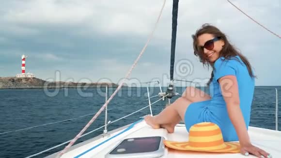 一位戴着黄色帽子穿着蓝色裙子的女士在海洋的夏季靠近灯塔的游艇上休息视频的预览图