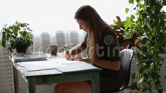 在家工作年轻漂亮的自由职业者正在房子窗户旁的桌子旁工作现代生态视频的预览图
