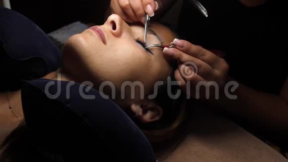 长睫毛的女人眼睫毛延伸用镊子粘合人造睫毛一个女人躺在化妆品上视频的预览图