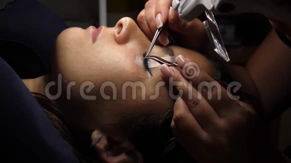 长睫毛的女人眼睫毛延伸用镊子粘合人造睫毛一个女人躺在化妆品上视频的预览图