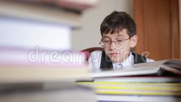 男孩坐在一张桌子旁桌上放着一叠书孩子读书戴眼镜的男孩视频的预览图