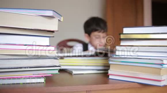 男孩坐在一张桌子旁桌上放着一叠书孩子读书戴眼镜的男孩视频的预览图