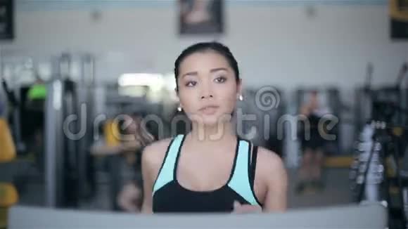 漂亮的亚洲女孩在健身房的跑步机上跑步全脸画像视频的预览图