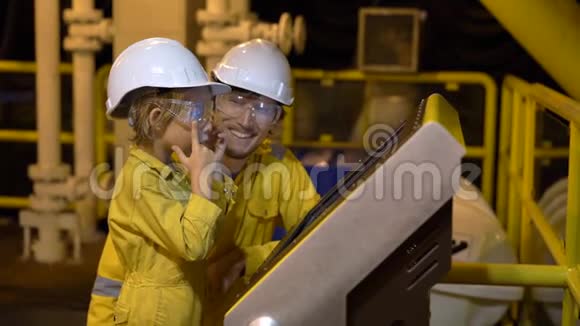 一个年轻人和一个小男孩都穿着黄色的工作服戴着眼镜戴着头盔在工业环境中戴着油视频的预览图