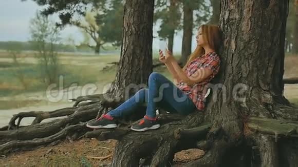 带着平板电脑的女孩坐在树上在户外慢动作视频的预览图