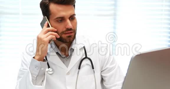 男性医生在电脑工作时用手机说话视频的预览图
