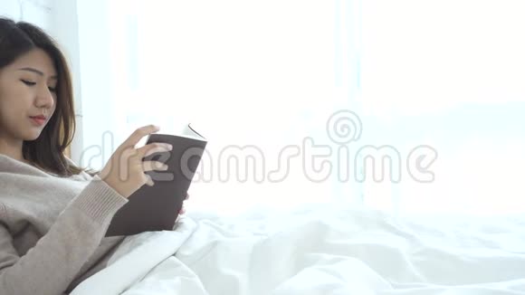 生活方式快乐的年轻亚洲女人躺在床上看书在家里穿着休闲服装视频的预览图