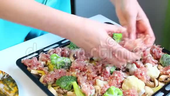 那个女人正在把肉末放在烤盘上上面已经放了切碎的蘑菇土豆和花椰菜视频的预览图
