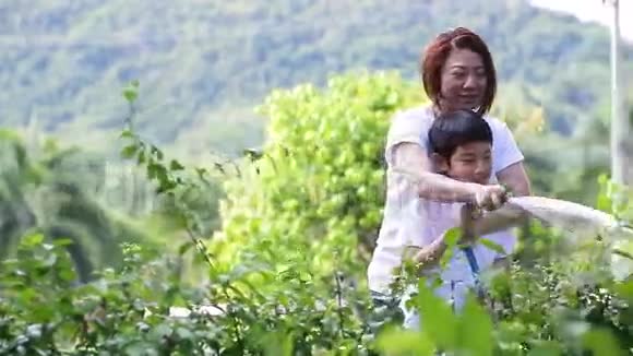 亚洲的母子正在给树浇水站在花园里的树荫下视频的预览图