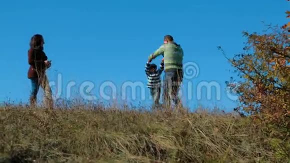 年轻的一家人在秋草甸散步视频的预览图