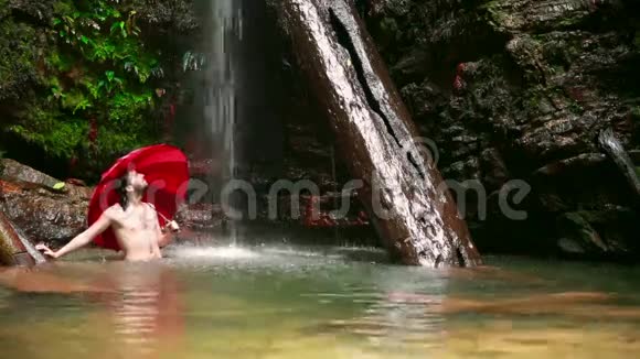 在婆罗洲热带雨林的瀑布中带着伞的人视频的预览图
