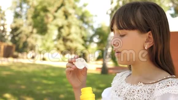 快乐的女孩在春天夏天和微笑的公园里吹着美丽的肥皂泡慢动作年轻女孩旅行视频的预览图