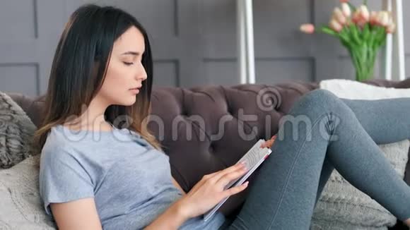沙发上用数码平板电脑的年轻女子视频的预览图