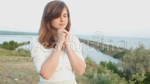 年轻美丽的女人在大自然中转向上帝女孩祈祷时双手交叉在下巴宗教观念视频的预览图