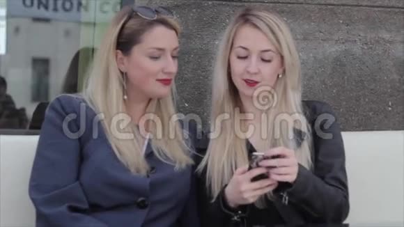 两个金发女郎坐在A咖啡馆里讨论智能手机上的照片视频的预览图