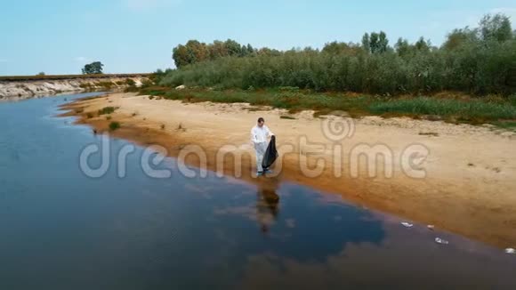 一个穿着防护服的人在干燥污染的河流岸边收集塑料垃圾的鸟瞰图视频的预览图
