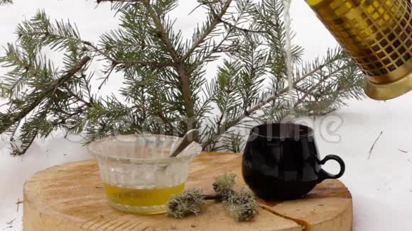 带蜂蜜的茶具把热茶从透明的茶壶倒到雪中的黑杯子视频的预览图