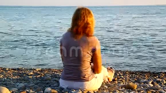 一个女人坐在海边的沙滩上扔石头视频的预览图