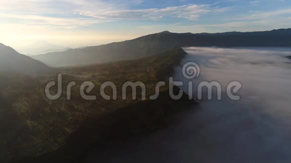 在晨雾中飞越CemoroLawang小村庄的空中观景航班视频的预览图