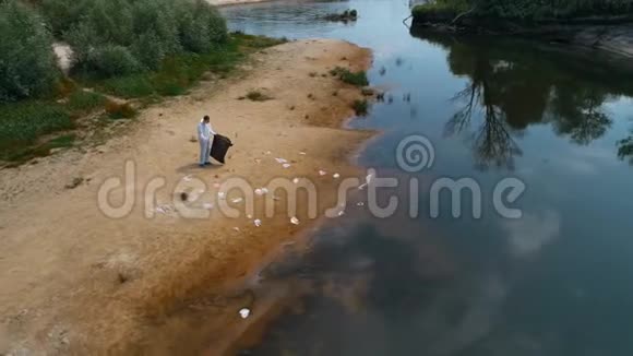 一个穿着防护服的人在干燥污染的河流岸边收集塑料垃圾的鸟瞰图视频的预览图