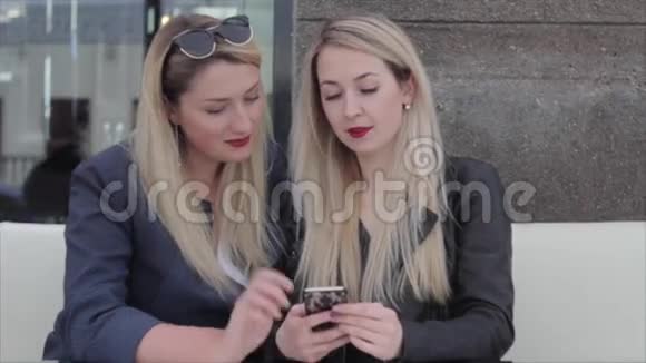 两个金发女郎坐在A咖啡馆里讨论智能手机上的照片视频的预览图