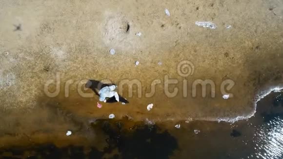 在干燥污染的河流岸边收集塑料垃圾的人穿着防护服和呼吸器的鸟瞰图视频的预览图