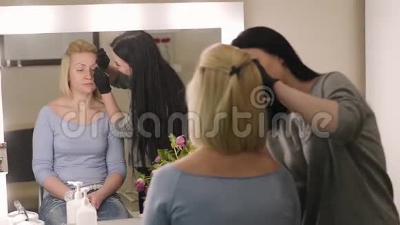 化妆师和模特年轻女子化妆师用专业的画笔给一个漂亮的女孩画眉毛视频的预览图