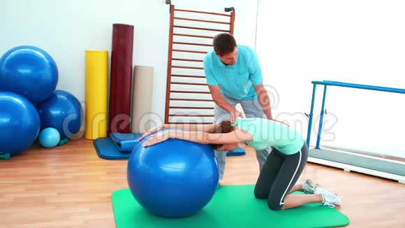 教练帮他的客户用健身球伸展背部视频的预览图