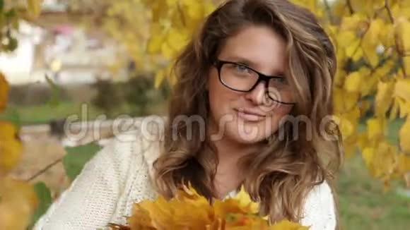 秋天公园里戴眼镜的女孩在树叶上特写视频的预览图