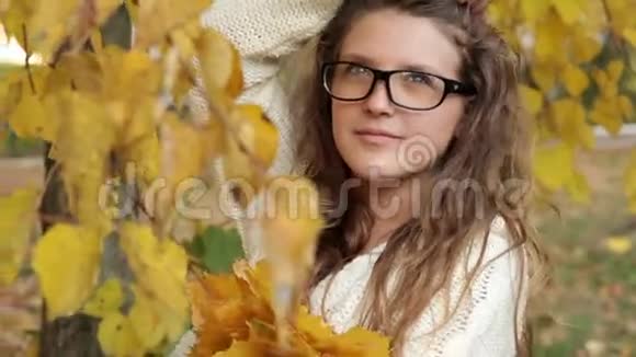 秋天公园里戴眼镜的女孩在树叶上特写视频的预览图