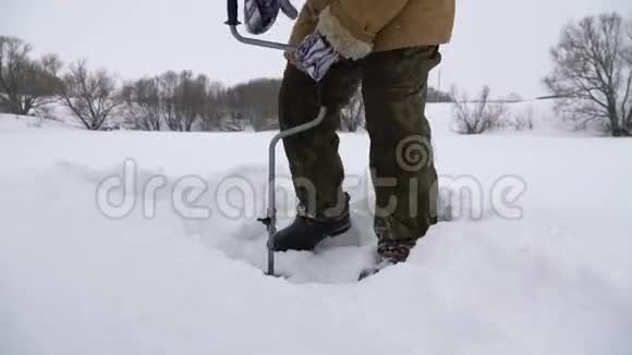 渔夫在白雪覆盖的湖面上钻了一个洞寻找一个好的钓鱼地点视频的预览图