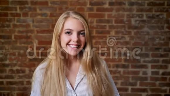 年轻的白人金发女孩微笑着看着镜头画像背景是砖墙视频的预览图