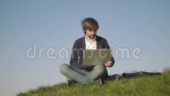 年轻人在公园的草地上使用笔记本电脑户外活动视频的预览图