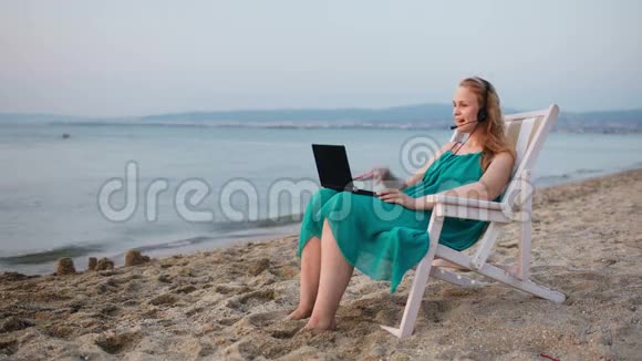 女人在海滩上放松手提电脑在说Skype视频的预览图