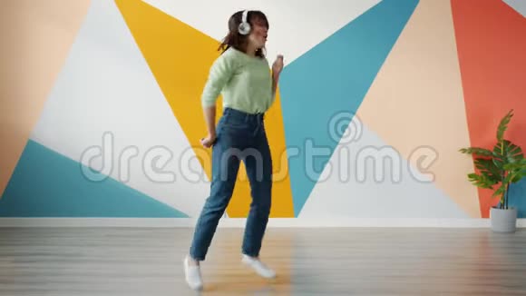 快乐的女孩跳舞在室内玩通过耳机听音乐视频的预览图