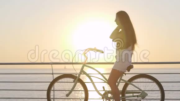日出或日落时年轻迷人的女士骑着老式自行车在海边视频的预览图