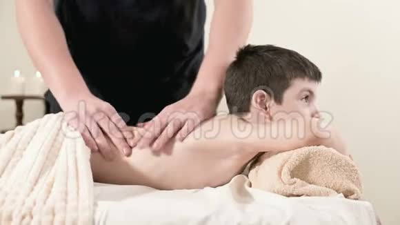 一位男性理疗师按摩师为躺在按摩床上的一个微笑的小男孩做一个疗愈放松的按摩按摩视频的预览图