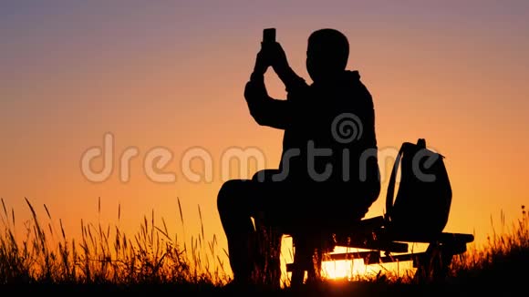 一个带背包的年轻游客使用手机在夕阳的光芒中慢动作旅行概念视频的预览图