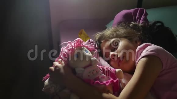 可爱的小女孩晚上睡在沙发床上拥抱她的娃娃女孩黑发少年室内可爱睡着了视频的预览图