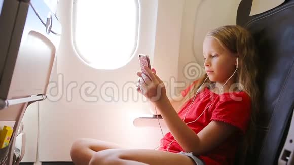 可爱的小女孩坐在靠窗的飞机上小孩坐在飞机窗前听音乐视频的预览图
