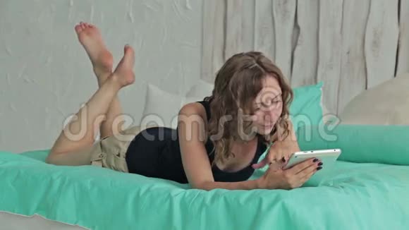 年轻卷曲的女人躺在床上拿着平板电脑多利射击视频的预览图