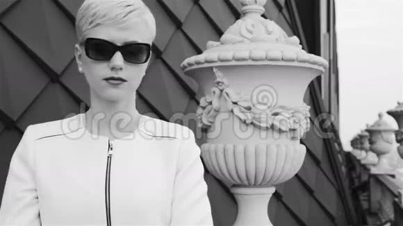 漂亮的金发女商人戴着太阳镜穿着白色夹克在电话城街道等着开会视频的预览图