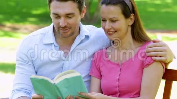 一对幸福的夫妇坐在公园的长椅上一起读书视频的预览图