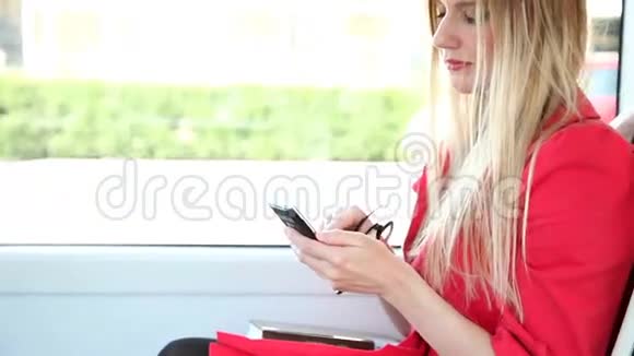年轻的金发女子骑着电车在手机电话手机上打字视频的预览图