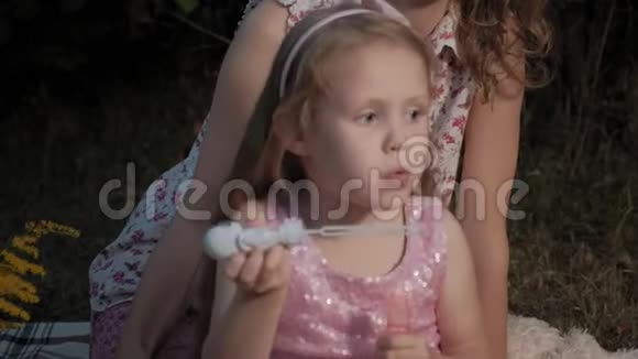 一对幸福的母女给肥皂泡充气一家人在城市公园里在日落的温暖的晚上野餐视频的预览图